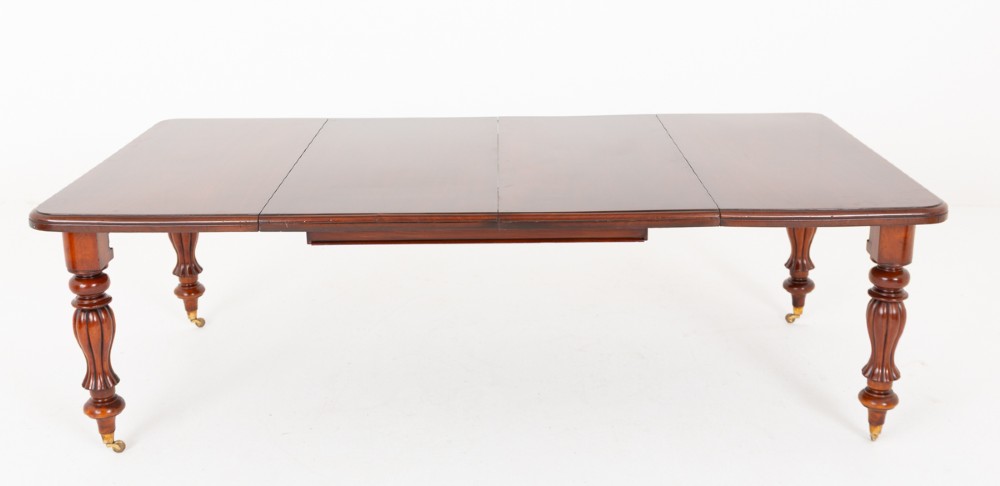 A Victorian mahogany extending dining table with two insertable leaves, fluted turned legs, and brass castors. View X
