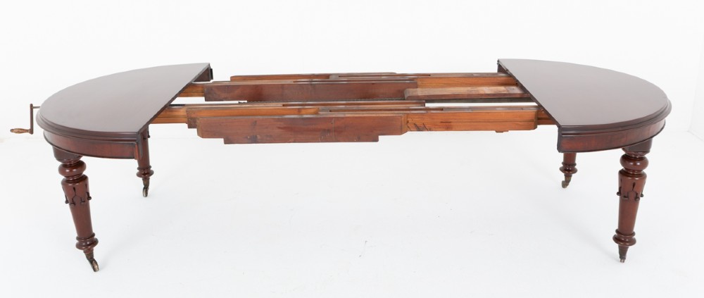 A William IV mahogany extending dining table with turned carved legs and brass castors set against a plain white background. View IV