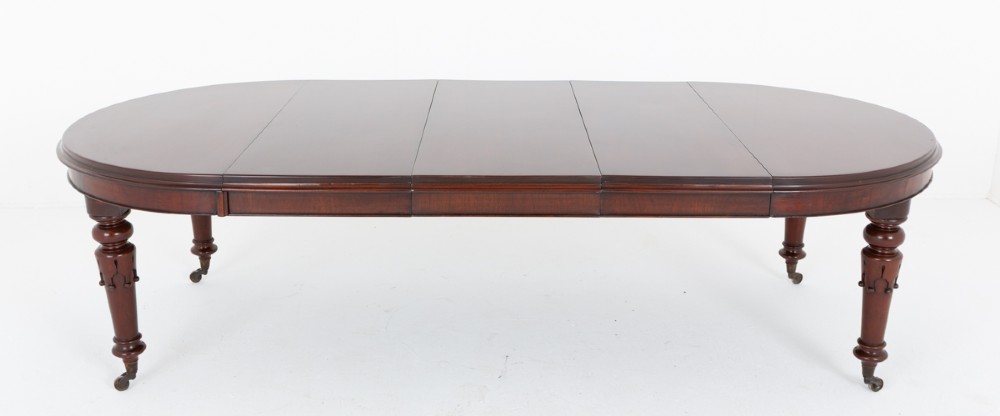 A William IV mahogany extending dining table with turned carved legs and brass castors set against a plain white background. View VI