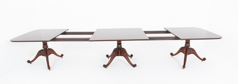 A large Regency style dark mahogany dining table featuring a three-pedestal base with carved splayed legs resting on brass castors. View IX