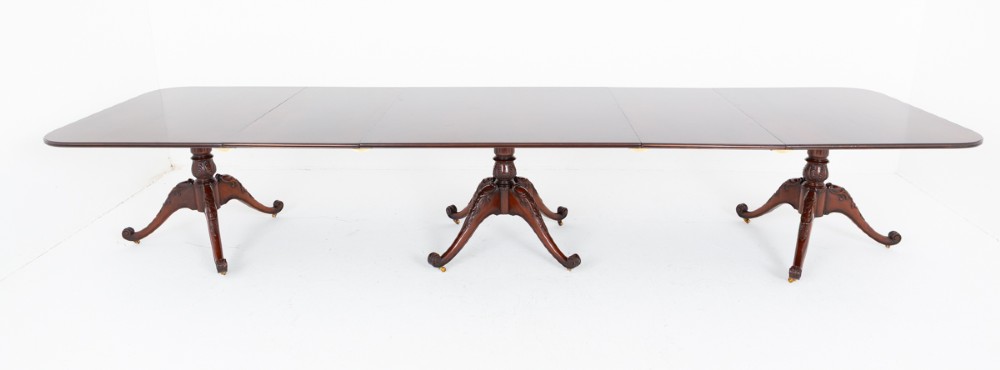 A large Regency style dark mahogany dining table featuring a three-pedestal base with carved splayed legs resting on brass castors. View X