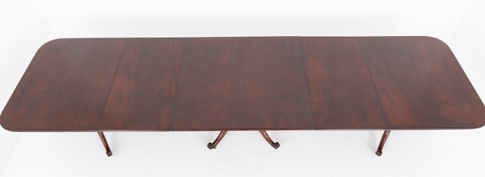 A large Regency style dark mahogany dining table featuring a three-pedestal base with carved splayed legs resting on brass castors. View XI