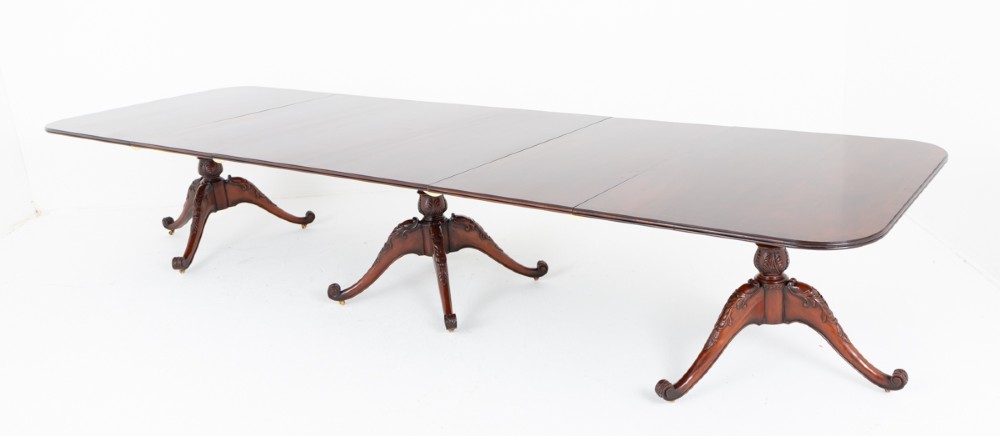 A large Regency style dark mahogany dining table featuring a three-pedestal base with carved splayed legs resting on brass castors.
