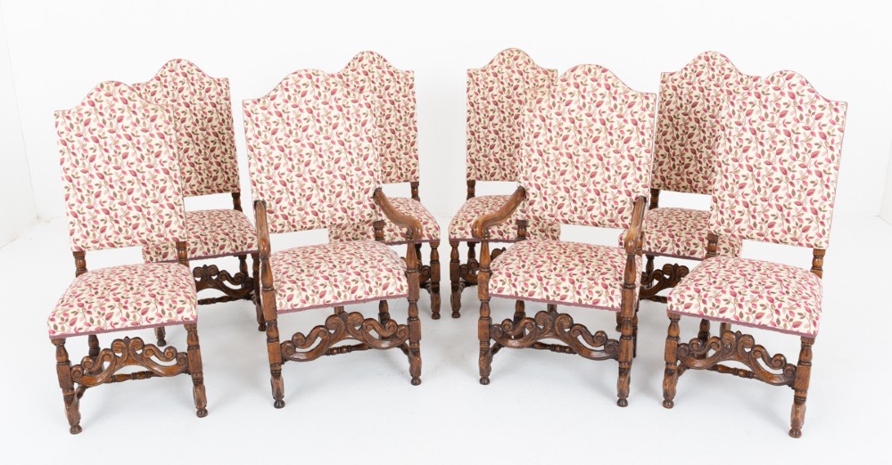 A set of eight Jacobean style oak dining chairs featuring carved scroll stretchers, turned legs, and floral leaf patterned fabric upholstery.