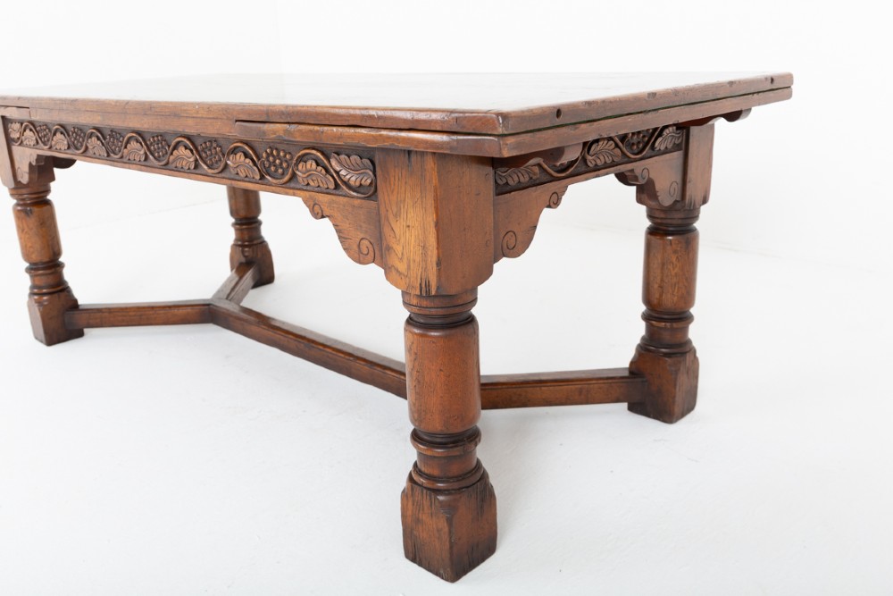 A dark oak Jacobean style extended refectory dining table featuring carved frieze detailing, turned legs, and lower stretchers. View V