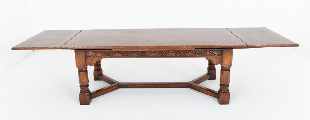 A dark oak Jacobean style extended refectory dining table featuring carved frieze detailing, turned legs, and lower stretchers. View VI