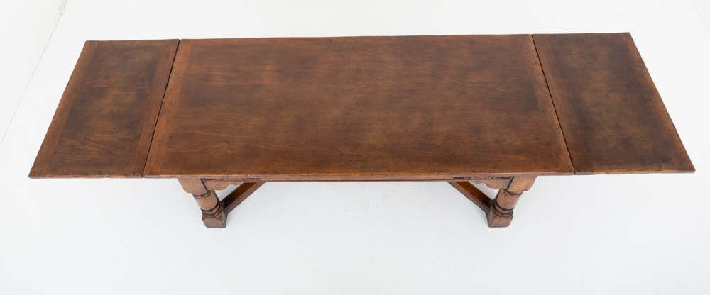 A dark oak Jacobean style extended refectory dining table featuring carved frieze detailing, turned legs, and lower stretchers. View VII