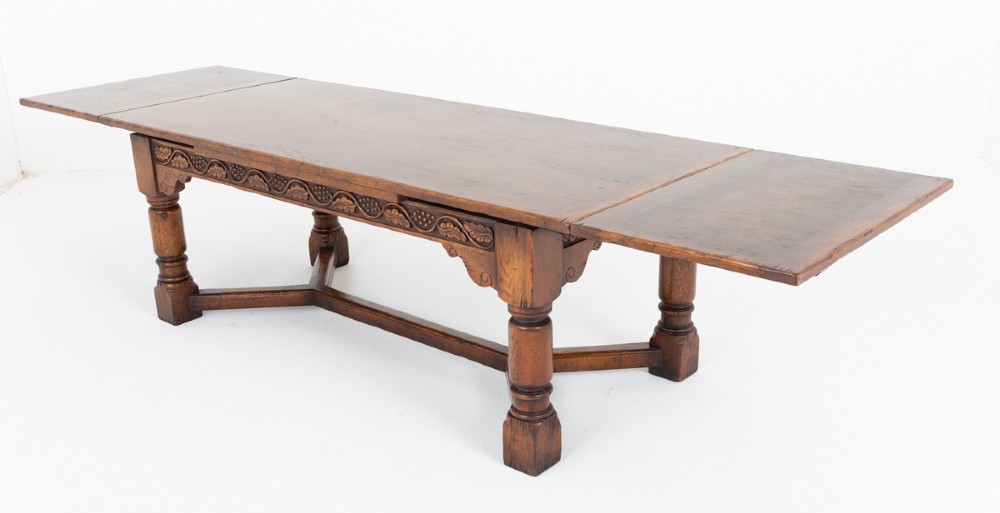 A dark oak Jacobean style extended refectory dining table featuring carved frieze detailing, turned legs, and lower stretchers.