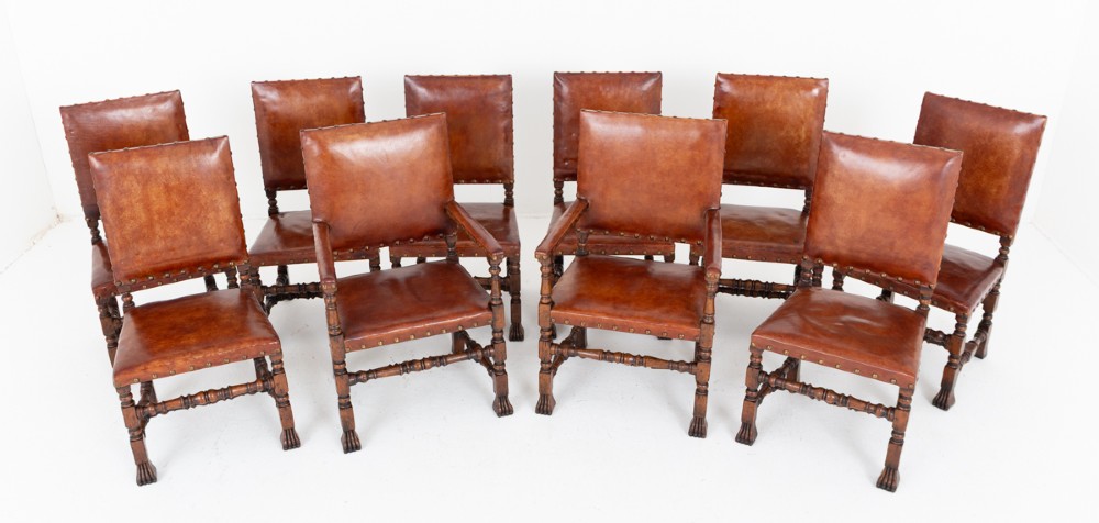 A set of ten brown leather upholstered oak dining chairs with brass studding and turned stretchers, including two carvers and eight side chairs.