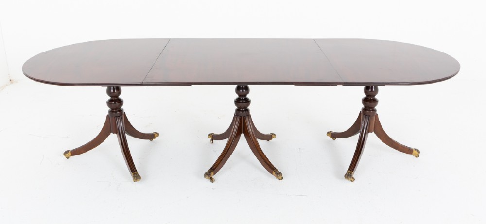 A large Regency Revival dark mahogany three-pedestal dining table with reeded splayed legs and brass claw castors. View II