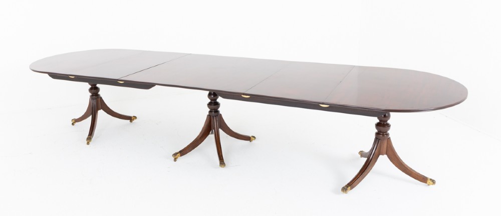 A large Regency Revival dark mahogany three-pedestal dining table with reeded splayed legs and brass claw castors.
