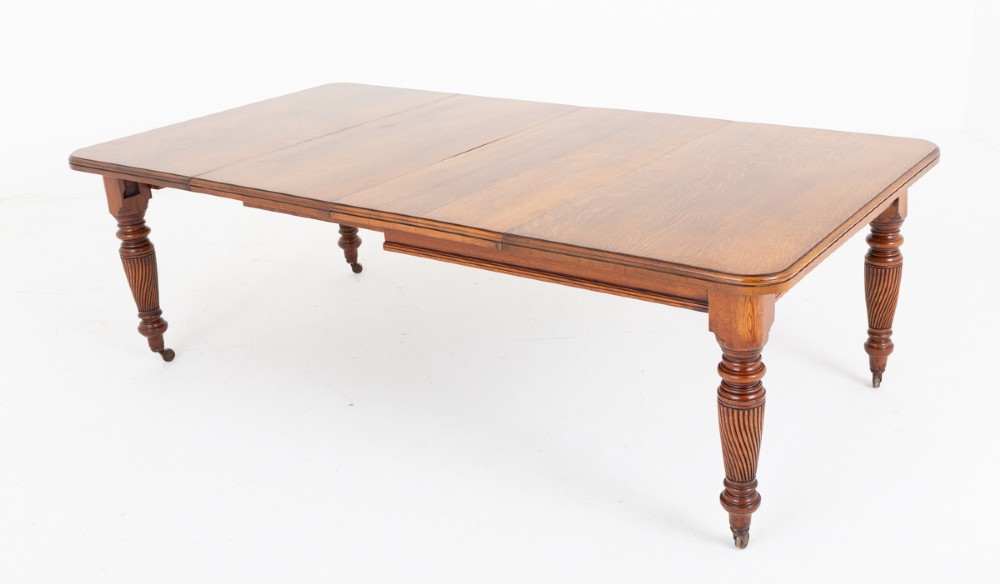 A Victorian blonde oak extending dining table featuring rounded corners, turned spiral-fluted legs, and brass castors against a white background.