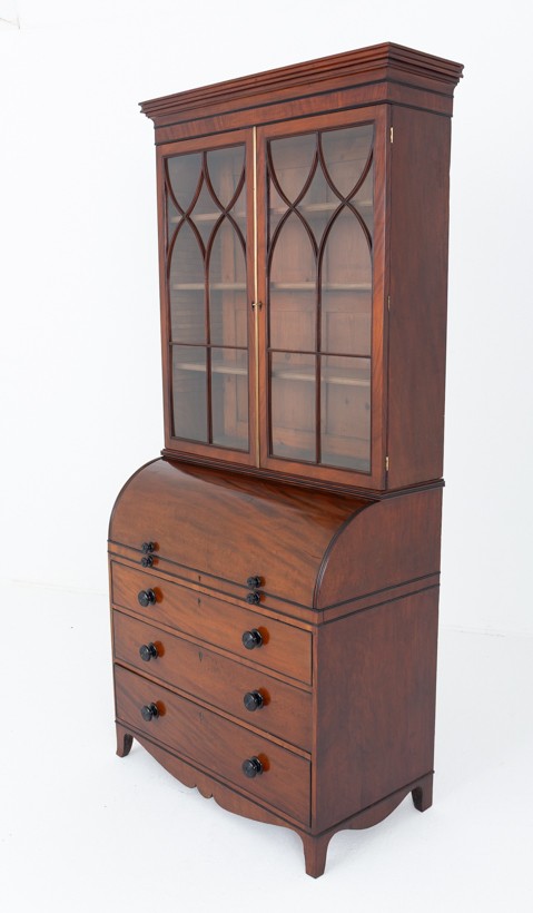 A Regency mahogany cylinder bureau bookcase featuring Gothic astragal glazed upper doors above a curved roll-top desk and three long drawers with turned dark handles.