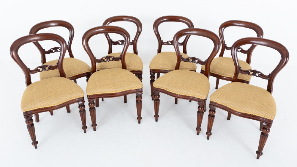 A set of eight Victorian style mahogany dining chairs with rounded balloon backs, carved mid-rails, gold upholstered seats, and fluted front legs. View II