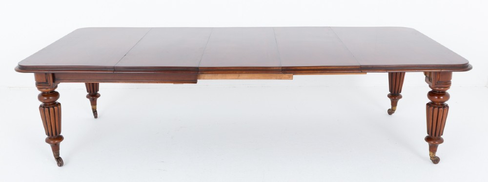 A William IV mahogany extending dining table with three additional leaves, standing on turned and reeded legs with brass castors.