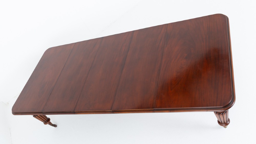 A William IV mahogany extending dining table with three additional leaves, standing on turned and reeded legs with brass castors. View VIII