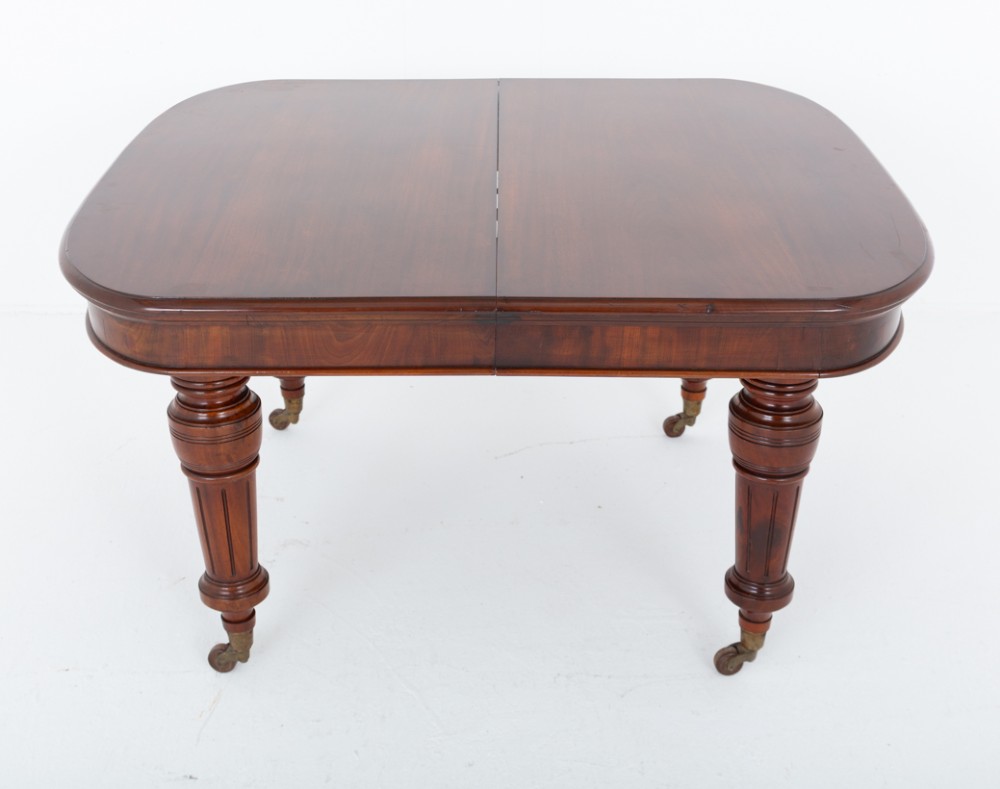 A Victorian mahogany extending dining table with two removable extension leaves, turned fluted legs, and brass castors. View II