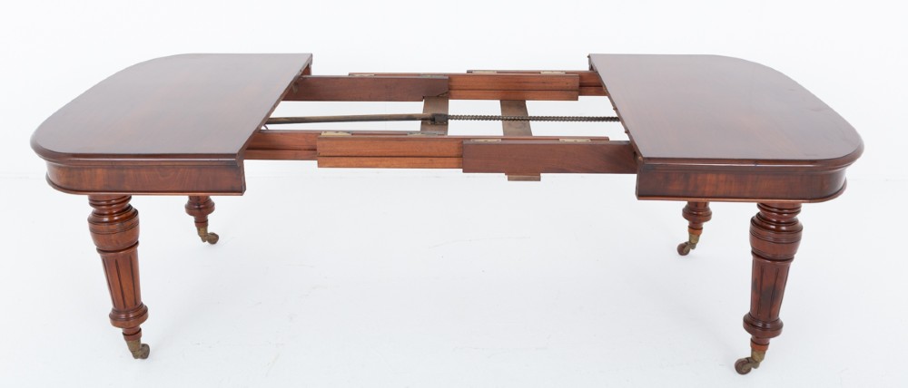 A Victorian mahogany extending dining table with two removable extension leaves, turned fluted legs, and brass castors. View V