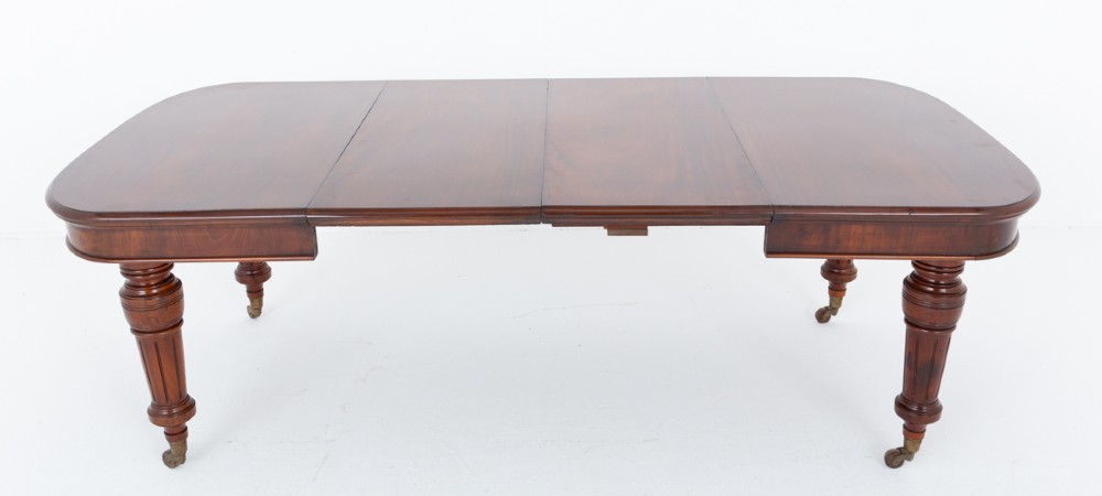 A Victorian mahogany extending dining table with two removable extension leaves, turned fluted legs, and brass castors. View VI