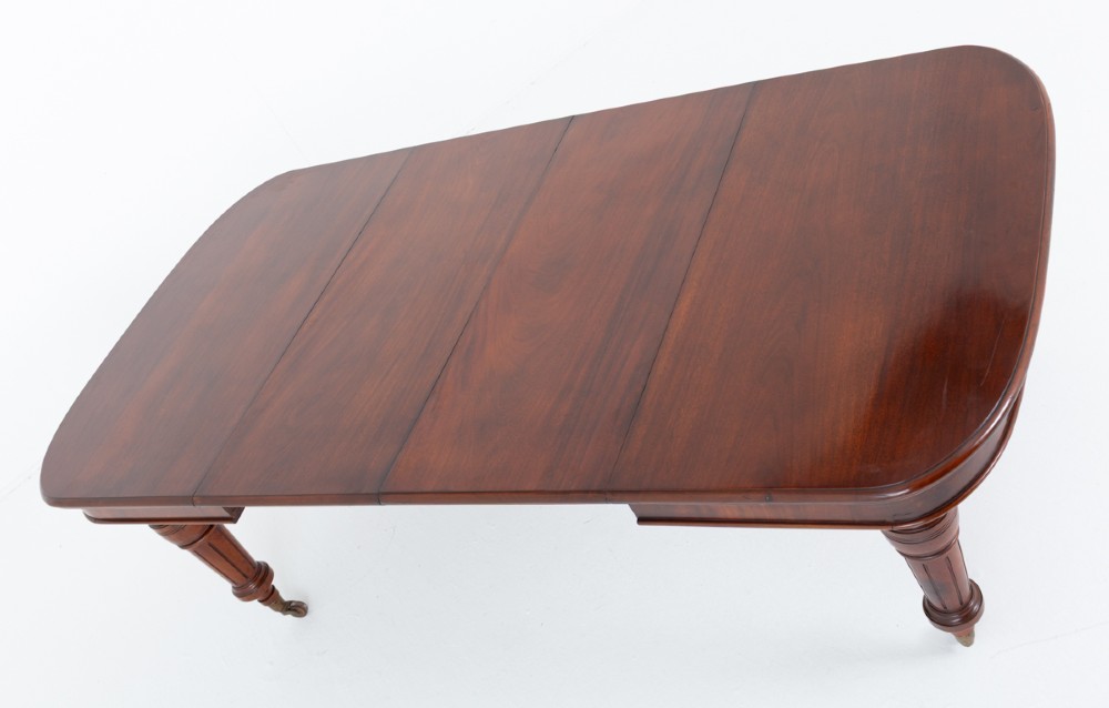A Victorian mahogany extending dining table with two removable extension leaves, turned fluted legs, and brass castors. View IX