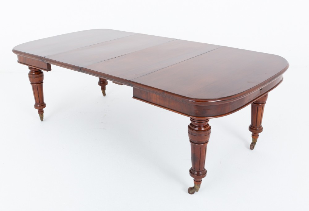 A Victorian mahogany extending dining table with two removable extension leaves, turned fluted legs, and brass castors. View X