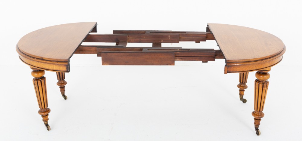A Victorian blonde oak extending dining table featuring turned fluted legs supported on metal castors. View IV