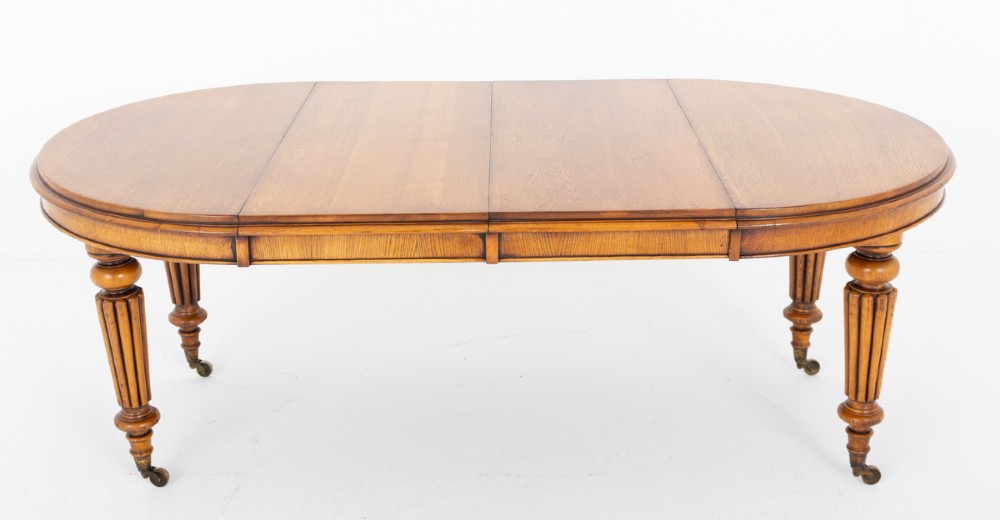 A Victorian blonde oak extending dining table featuring turned fluted legs supported on metal castors. View V