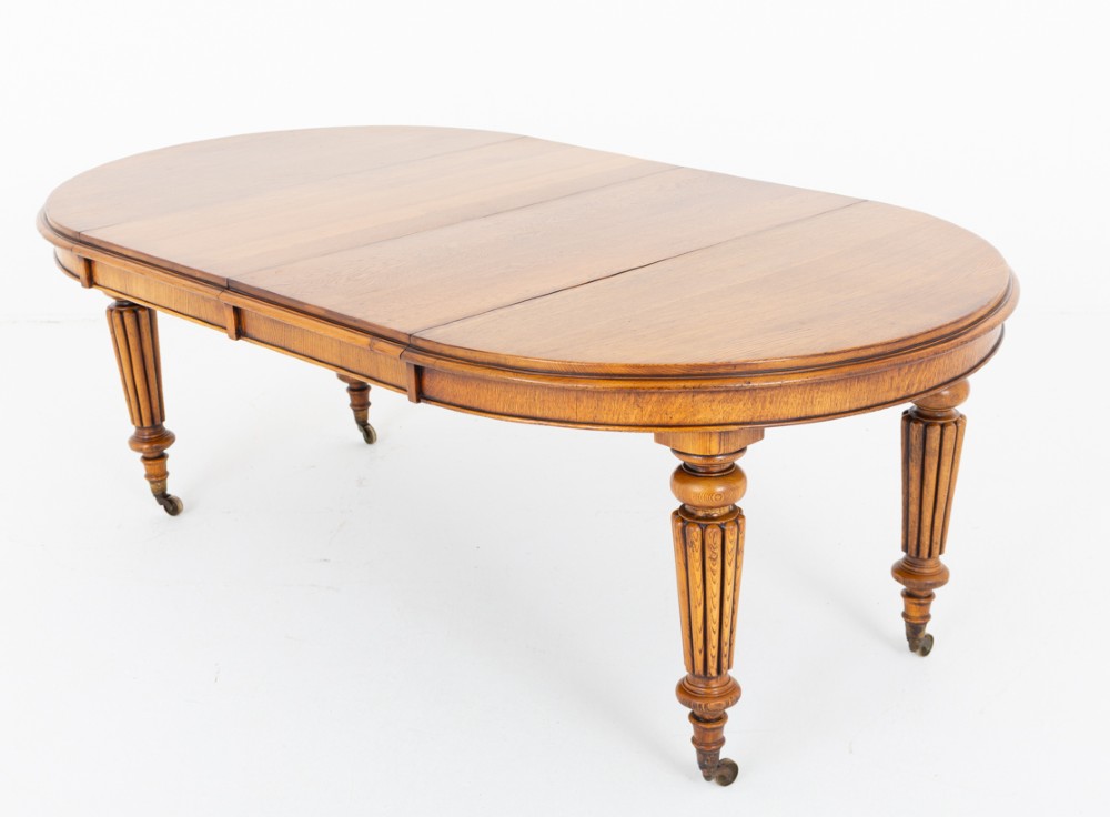 A Victorian blonde oak extending dining table featuring turned fluted legs supported on metal castors.