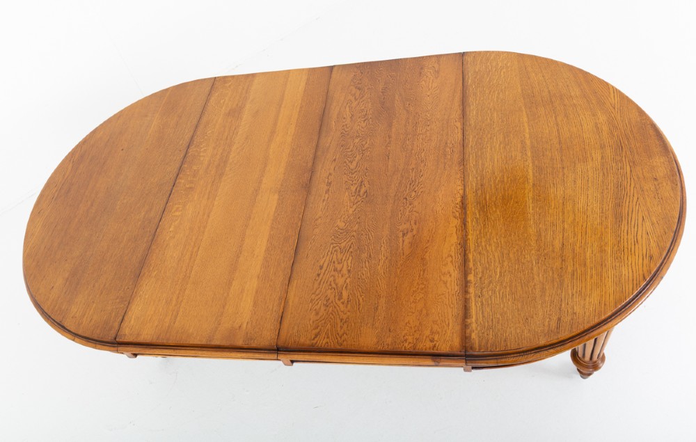 A Victorian blonde oak extending dining table featuring turned fluted legs supported on metal castors. View VII