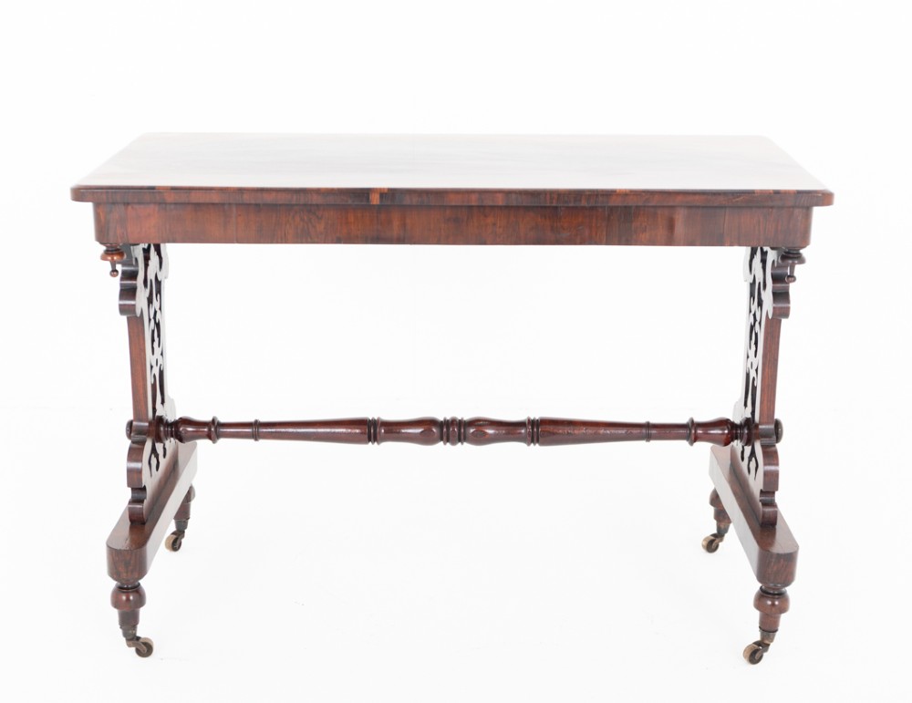 A mid-19th century Victorian rosewood stretcher table featuring a rectangular polished top, openwork pierced end supports, a turned central stretcher, and brass castors. View II