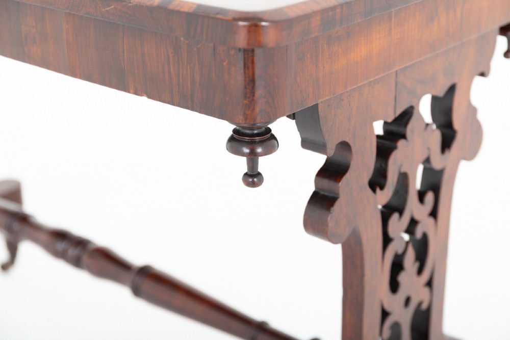 A mid-19th century Victorian rosewood stretcher table featuring a rectangular polished top, openwork pierced end supports, a turned central stretcher, and brass castors. View IV