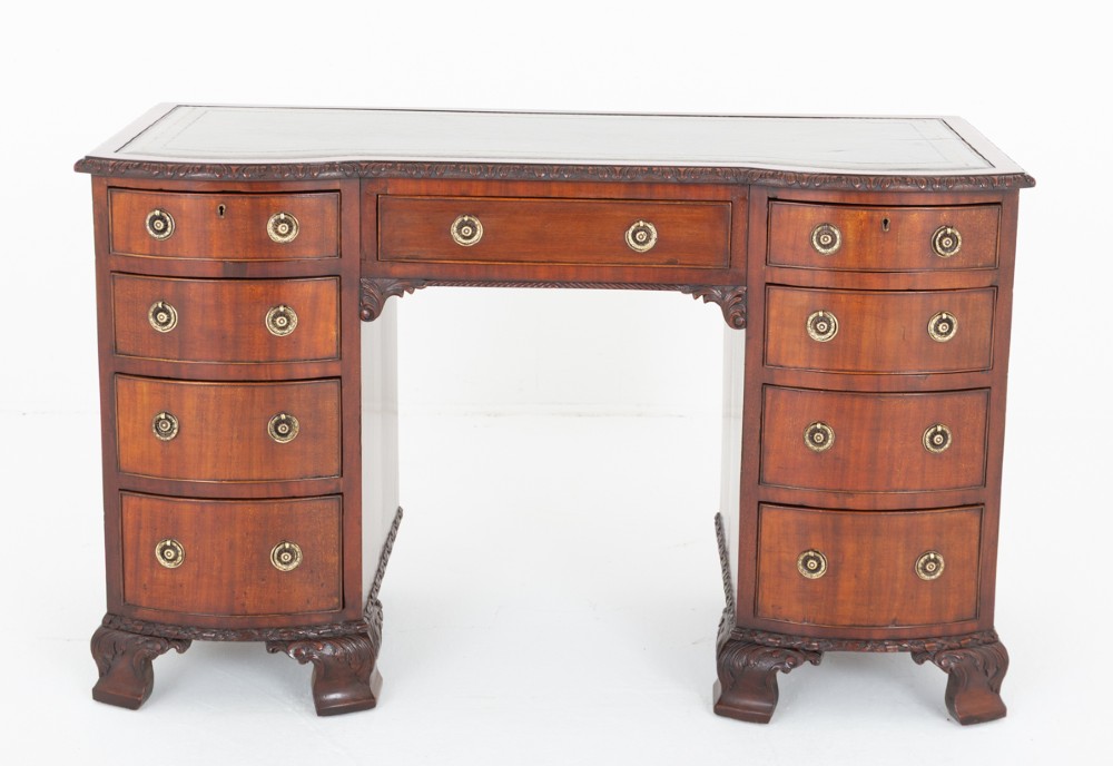 A Georgian Revival mahogany pedestal desk featuring a leather-lined top, curved drawer fronts with brass ring handles, and carved bracket feet. View II