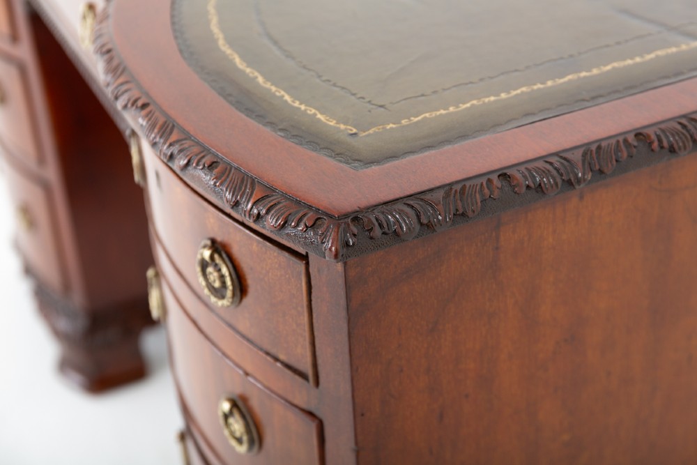 A Georgian Revival mahogany pedestal desk featuring a leather-lined top, curved drawer fronts with brass ring handles, and carved bracket feet. View V