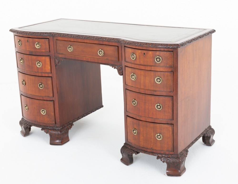 A Georgian Revival mahogany pedestal desk featuring a leather-lined top, curved drawer fronts with brass ring handles, and carved bracket feet. View IX