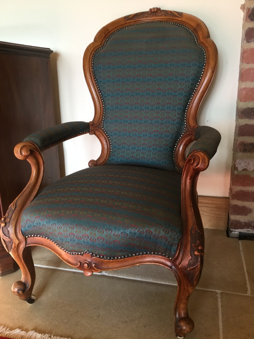 A Victorian carved walnut open armchair upholstered in patterned teal fabric with cabriole legs and front castors. View II