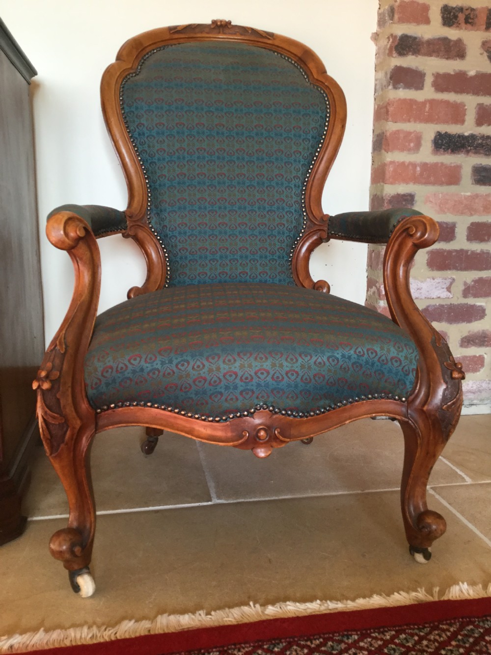 A Victorian carved walnut open armchair upholstered in patterned teal fabric with cabriole legs and front castors. View IV