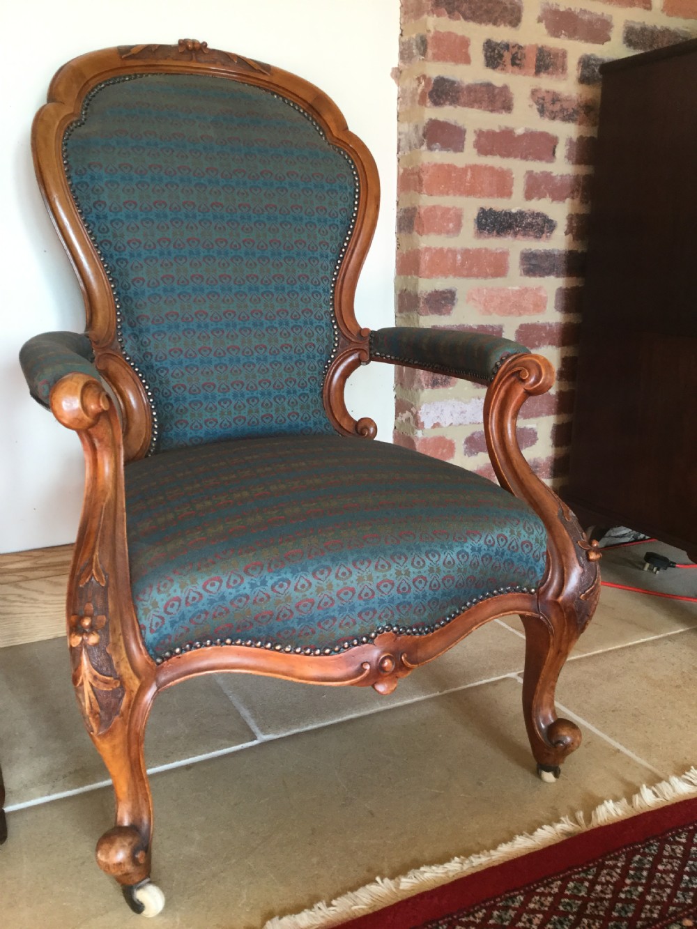 A Victorian carved walnut open armchair upholstered in patterned teal fabric with cabriole legs and front castors. View V