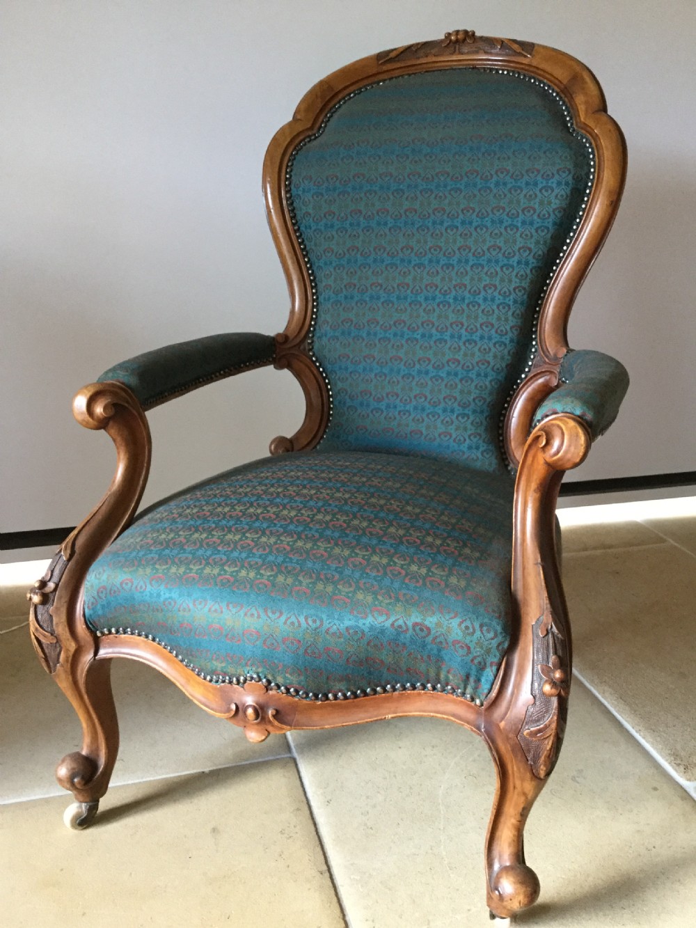 A Victorian carved walnut open armchair upholstered in patterned teal fabric with cabriole legs and front castors.