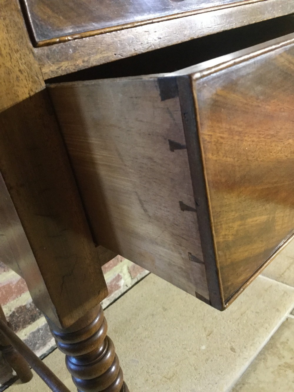 A Victorian mahogany writing table featuring turned legs, five drawers with wooden knob handles, and carved kneehole arch details. View IV