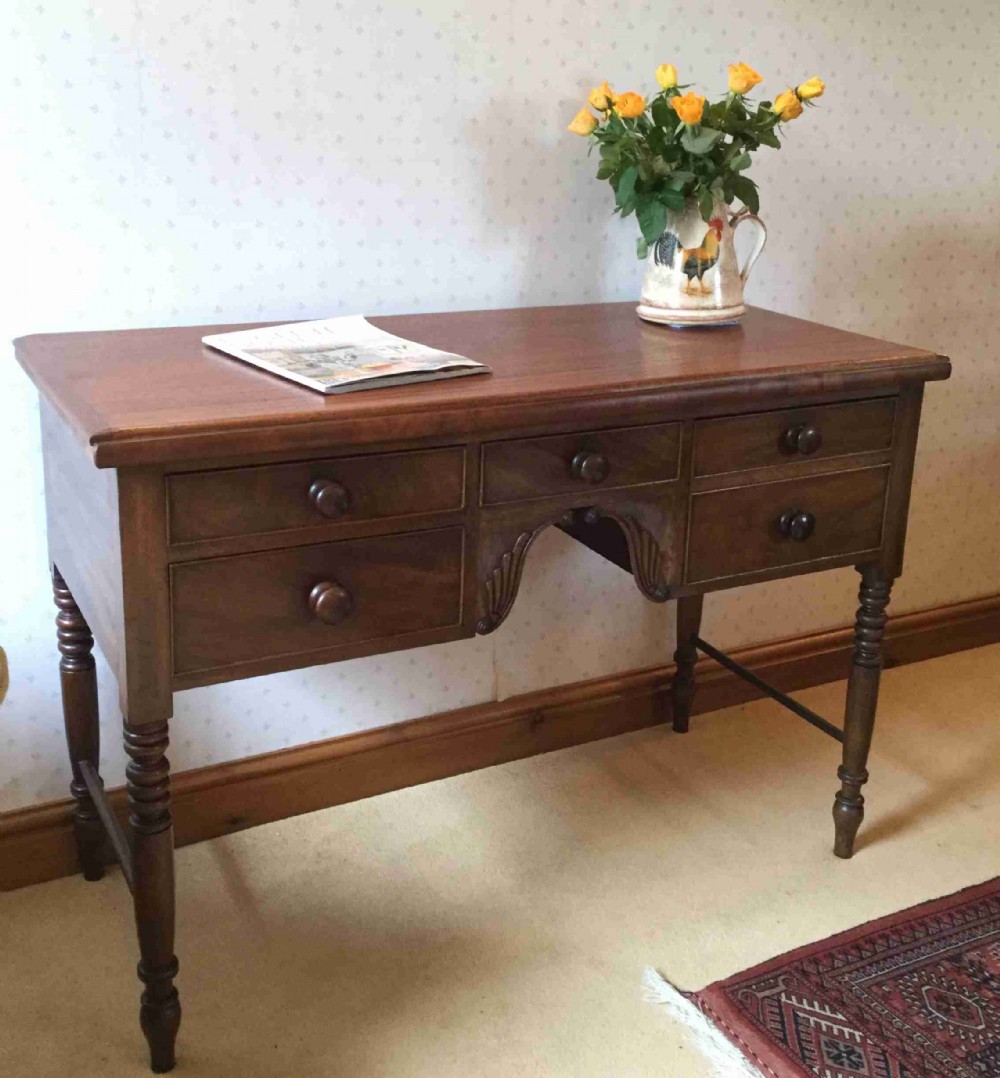A Victorian mahogany writing table featuring turned legs, five drawers with wooden knob handles, and carved kneehole arch details.