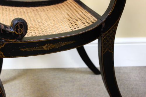 A pair of ebonised Regency armchairs featuring woven cane seats and backrests, swept armrests, and front sabre legs. View IV