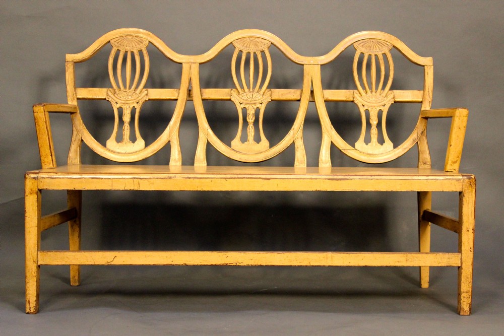 A nineteenth-century painted mahogany sofa featuring a triple chair-back design with carved vase-shaped splats, straight armrests, and squared legs.