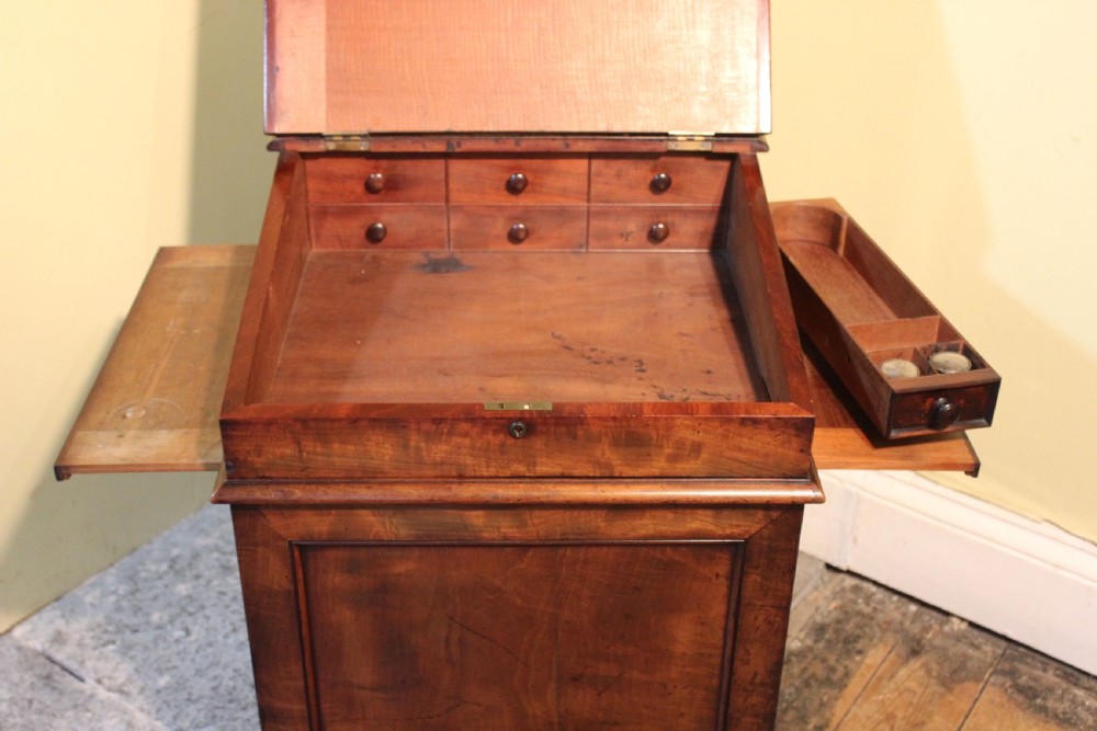 An early 19th-century mahogany Davenport desk featuring a sloped leather writing surface, a brass top gallery rail, and four side drawers with turned wooden knobs. View IV