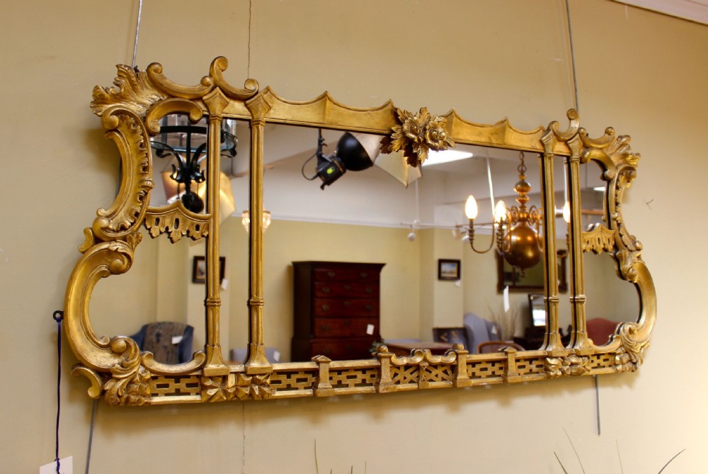 A horizontal 19th-century giltwood overmantel mirror featuring carved floral cresting, vertical column supports, and geometric fretwork along the base. View II