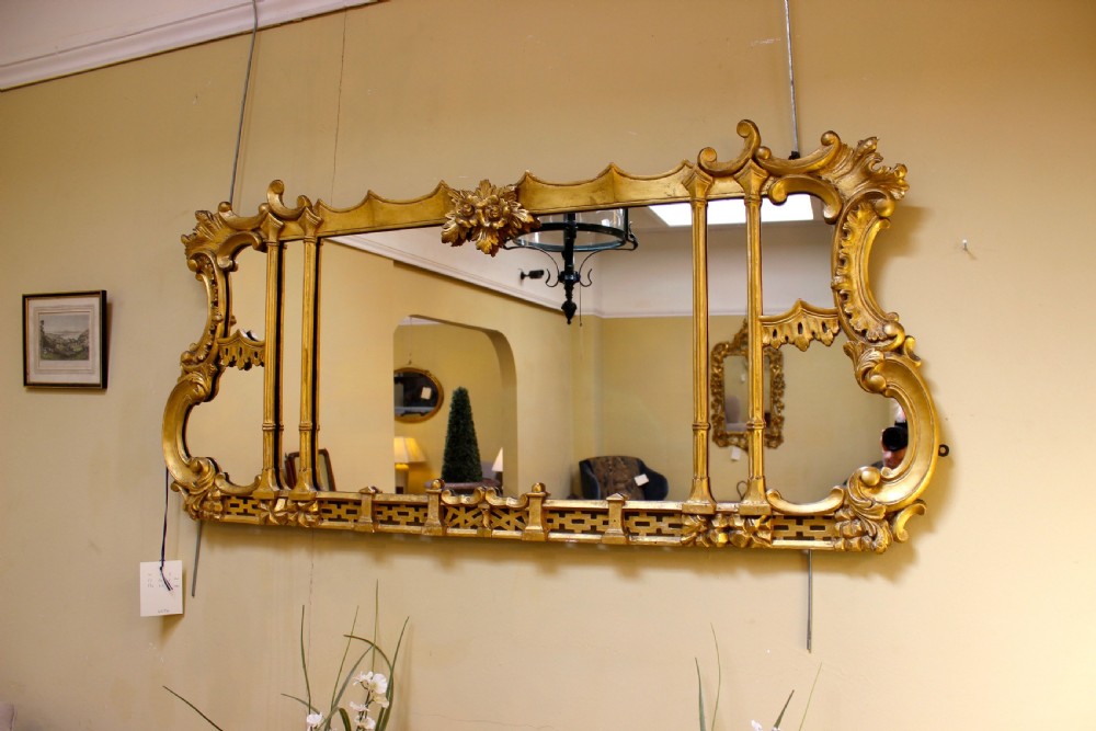 A horizontal 19th-century giltwood overmantel mirror featuring carved floral cresting, vertical column supports, and geometric fretwork along the base. View III