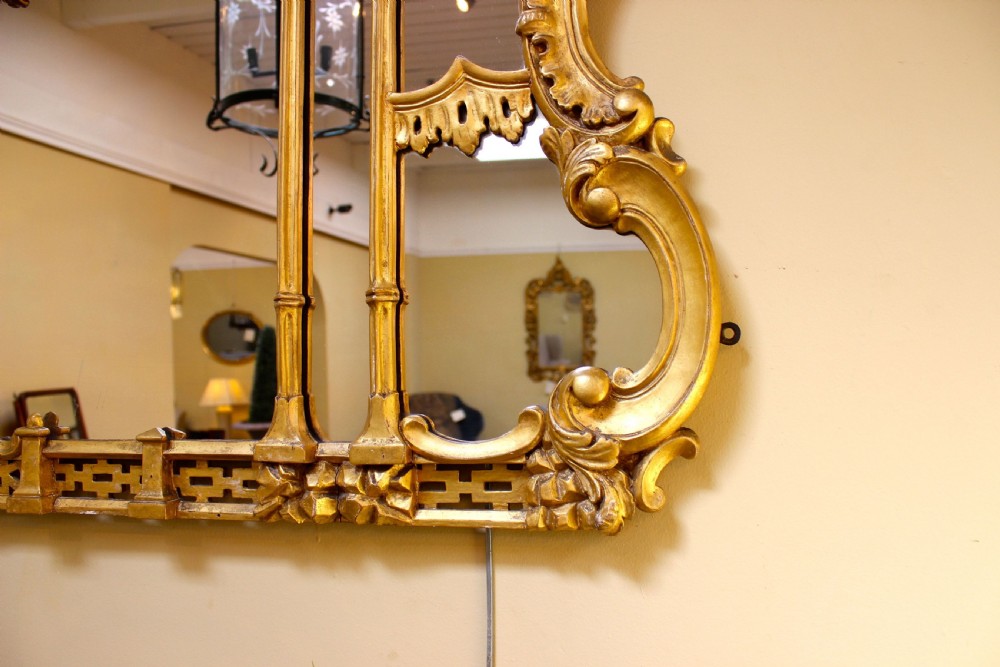A horizontal 19th-century giltwood overmantel mirror featuring carved floral cresting, vertical column supports, and geometric fretwork along the base. View IV