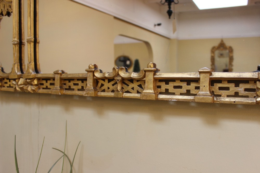 A horizontal 19th-century giltwood overmantel mirror featuring carved floral cresting, vertical column supports, and geometric fretwork along the base. View VI