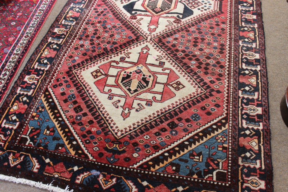 A hand-knotted antique Persian wool carpet featuring three large diamond medallions set across a detailed red patterned field framed by dark blue borders. View III