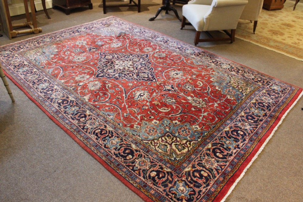 A hand-knotted oriental wool rug with a dark navy central medallion and arabesque scroll motifs set against a red background.