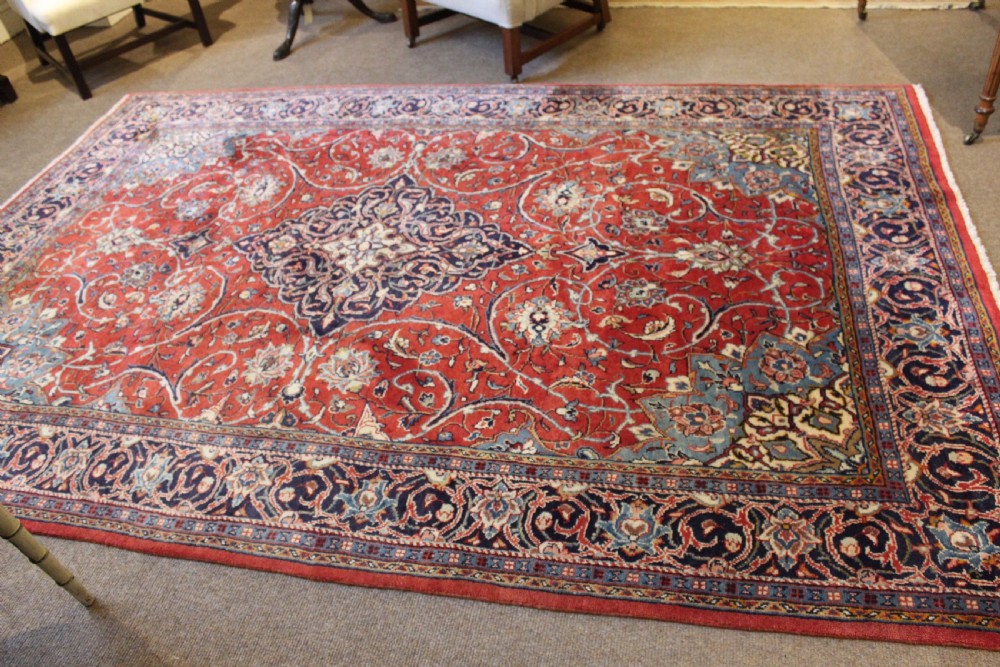 A hand-knotted oriental wool rug with a dark navy central medallion and arabesque scroll motifs set against a red background. View II